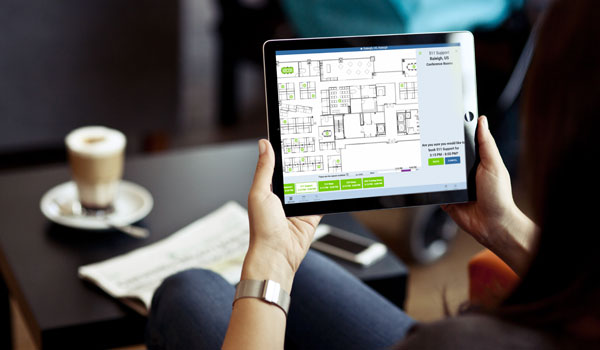 A businesswoman holding a tablet with a floor plan on the screen.