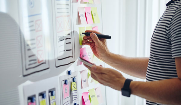 Man drawing a diagram on a whiteboard with several sticky notes around it.